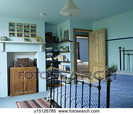 Stock Photography - Storage chest in fireplace of pale blue bedroom with black cast-ion bed. Fotosearch