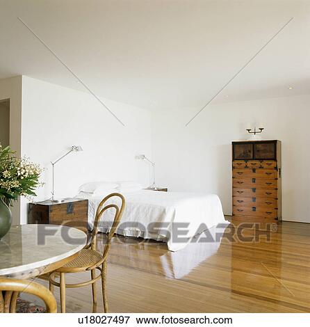 Stock Photo - Table and chairs in modern white bedroom with wooden flooring. Fotosearch