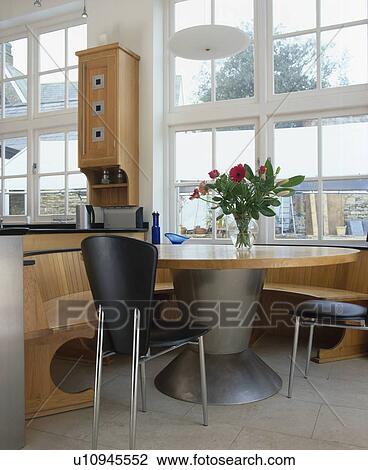Stock Image - Table with steel pedestal and black chairs in dining area with fitted wooden seating. Fotosearch