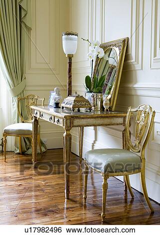Tall glass lamp on antique desk in cream panelled drawing room with gilt-framed chairs and polished floorboards View Large Photo Image Stock Photograph - Tall glass lamp on antique desk in cream panelled drawing room with gilt-framed chairs and polished floorboards. Fotosearch
