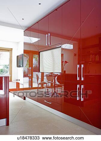 Stock Image - Tambour shutter on storage unit in shiny red fitted storage cupboards in modern kitchen. Fotosearch