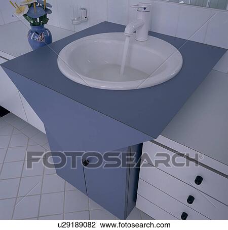 Tap with water pouring into white basin in modern blue vanity unit View Large Photo Image Stock Image - Tap with water pouring into white basin in modern blue vanity unit. Fotosearch