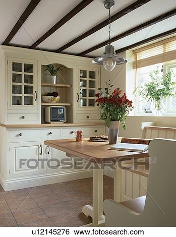 Television on fitted cream dresser in small cottage dining room with wooden table and bench seating View Large Photo Image Stock Photograph - Television on fitted cream dresser in small cottage dining room with wooden table and bench seating. Fotosearch