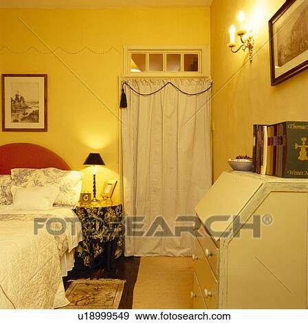 Tented wardrobe in small yellow bedroom with lighted lamp on bedside table View Large Photo Image Stock Photo - Tented wardrobe in small yellow bedroom with lighted lamp on bedside table. Fotosearch