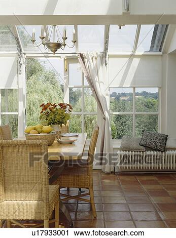 Stock Image - Terracotta tiled floor in conservatory dining room with wicker chairs&#10;. Fotosearch