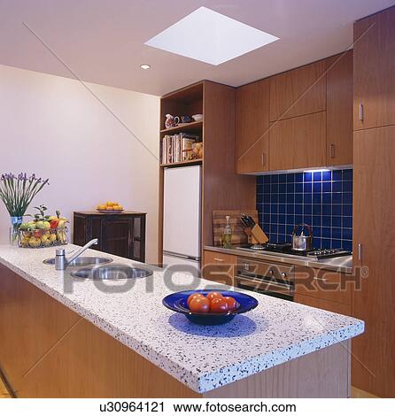 Stock Image - Terrazzo-tiled worktop on island unit in modern kitchen with fitted wood units. Fotosearch
