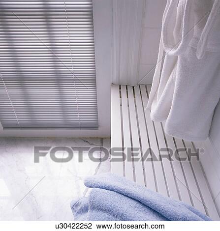 Stock Image - Towelling bathroom above slatted white seat in modern bathroom. Fotosearch