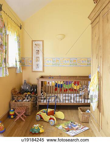 Stock Photography - Toys on floor beside wooden cot in baby's pastel yellow nursery bedroom with wooden flooring. Fotosearch