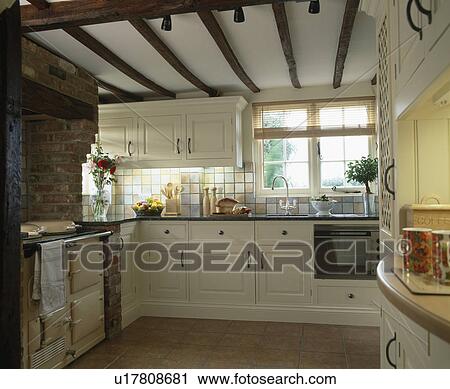 Stock Image - Traditional cream cottage kitchen with beamed ceiling and Aga oven. Fotosearch