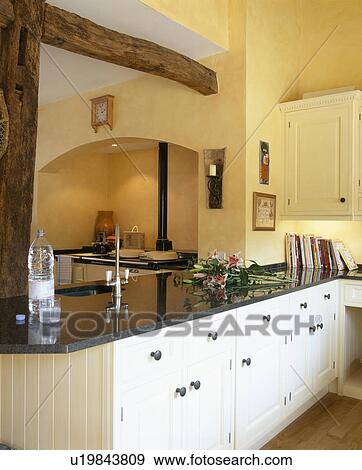 Stock Photo - Traditional yellow country kitchen with large beam above cream fitted unit. Fotosearch