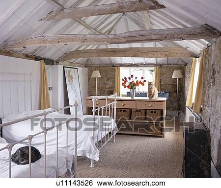 Twin white cast iron beds in country loft conversion bedroom with beamed apex roof View Large Photo Image Stock Photograph - Twin white cast iron beds in country loft conversion bedroom with beamed apex roof. Fotosearch