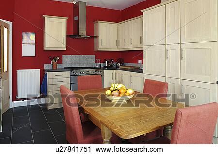 Stock Image - Upholsted chairs and wood table in red kitchen with pale wood units. Fotosearch