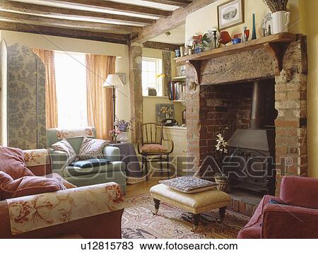 Upholstered stool in front of black iron stove in brick fireplace in cream cottage living room View Large Photo Image Stock Image - Upholstered stool in front of black iron stove in brick fireplace in cream cottage living room . Fotosearch