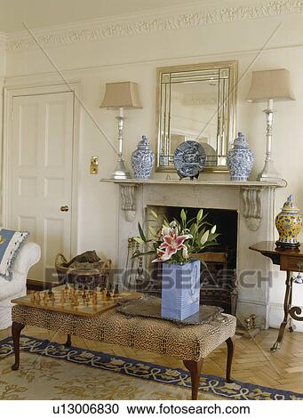 Stock Image - Upholstered stool in front of fireplace in tradtional country living room. Fotosearch