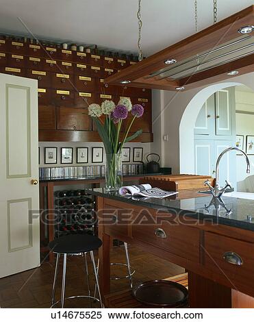 Stock Photography - Vase of alliums on island unit in modern kitchen with wall-mounted antique drawers. Fotosearch