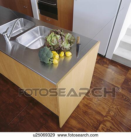 Stock Photo - Vegetables on stainless steel worktop on island unit with double steel sinks. Fotosearch