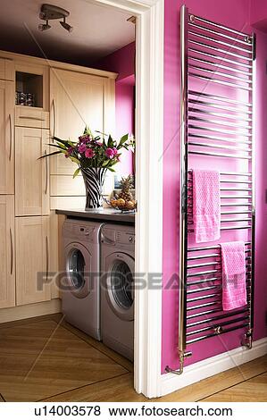 Stock Photo - Vertical metal radiator on pink wall beside doorway to utility room with washing machine and tumble dryere. Fotosearch