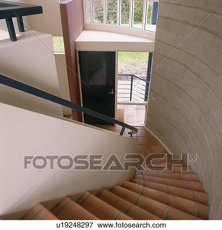 Stock Photo - View down terracotta tiled staircase with curved wall to large modern hall. Fotosearch