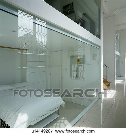 Stock Photo - View from hall through glass wall to bed with white linen in modern bedroom. Fotosearch