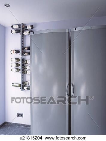 Picture - Wall mounted wine storage rack beside large grey American style fridge freezer in modern kitchen. Fotosearch