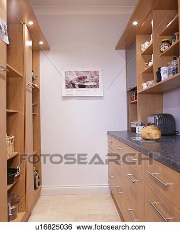 Stock Photograph - Wall shelves above fitted units on either side of modern galley kitchen. Fotosearch