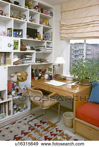Stock Photo - Wall-to-ceiling cube shelving in study bedroom with chair and small wooden desk in front of window with cream blind . Fotosearch