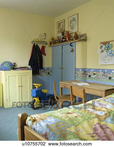 Stock Image - Wallpaper frieze and blue carpet in child's pastel yellow bedroom with fitted blue storage cupboard. Fotosearch