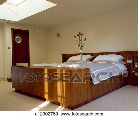 Stock Photo - Walnut bed with white and grey bedlinen in modern attic bedroom. Fotosearch