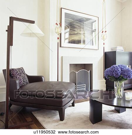 Stock Image - White and black standard lamp above black leather chaiselongue in white living room with black coffee table. Fotosearch