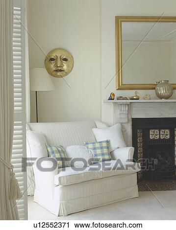 White and checked cushions on small white sofa beside fireplace in white living room with gilt sun sculpture on wall View Large Photo Image Stock Image - White and checked cushions on small white sofa beside fireplace in white living room with gilt sun sculpture on wall. Fotosearch