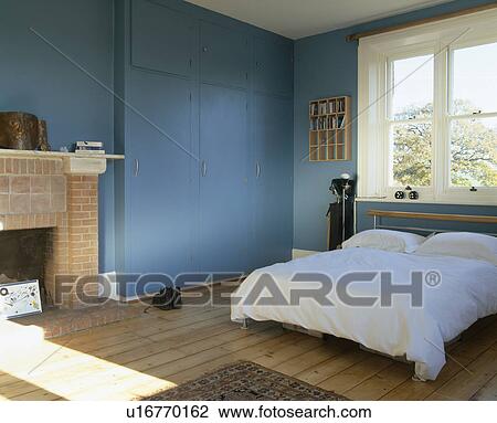 Stock Image - White bedlinen on bed in blue bedroom with wooden flooring. Fotosearch