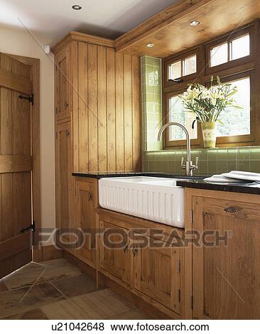 Stock Photo - White Belfast sink in country kitchen with fitted oak cupboards. Fotosearch