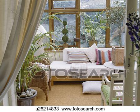 Stock Image - White chaiselongue belows window in conservatory living room. Fotosearch
