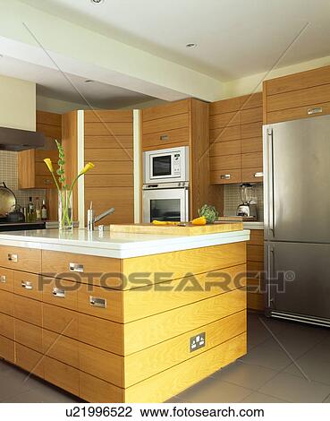 Stock Image - White Corian worktop on pale wood island unit in modern kitchen. Fotosearch