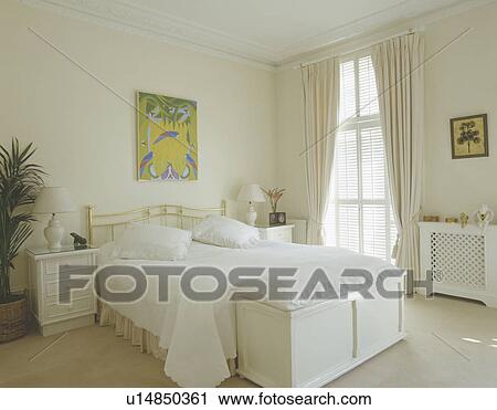 Stock Image - White cushions and quilt on bed in white bedroom with white wooden chest . Fotosearch