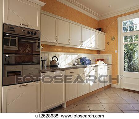 Stock Photography - White fitted units in modern orange kitchen. Fotosearch