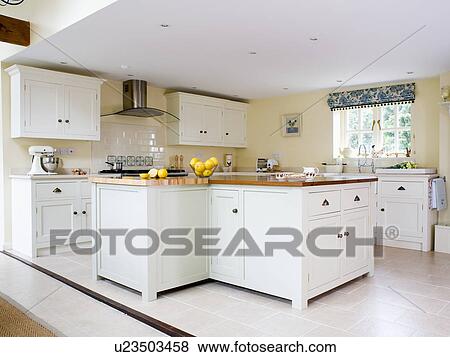 Stock Photo - White fitted units in pale yellow country kitchen with limestone flooring. Fotosearch
