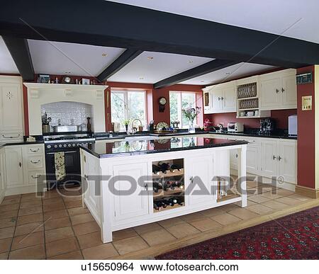 Picture - White island unit with integral wine storage in beamed country kitchen with quary tiled floor. Fotosearch