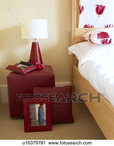 Stock Image - White lamp on brown upholstered stool used as bedside table. Fotosearch