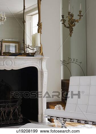 Stock Photo - White Mies van der Rohe Barcelona chair beside marble fireplace with antique overmantel mirror. Fotosearch