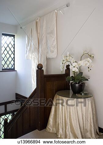 Picture - White orchid in pot on circular table with beige silk cloth on cottage landing with white kimono on the wall. Fotosearch
