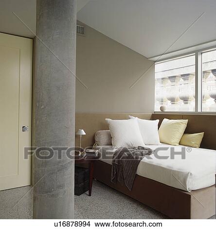Picture - White pillows and neutral linen on bed in modern city bedroom with concrete pillar. Fotosearch