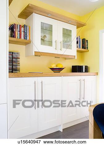 Stock Photo - White wall-cupboard with glazed doors in modern yellow kitchen with white fitted units. Fotosearch