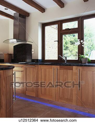 Window above fitted cupboards with blue halogen lighting below kickboards in modern country kitchen View Large Photo Image Picture - Window above fitted cupboards with blue halogen lighting below kickboards in modern country kitchen. Fotosearch