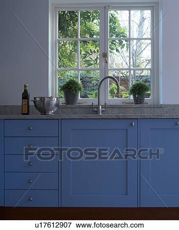 Stock Photo - Window above sink with chrome tap in fitted blue kitchen unit. Fotosearch
