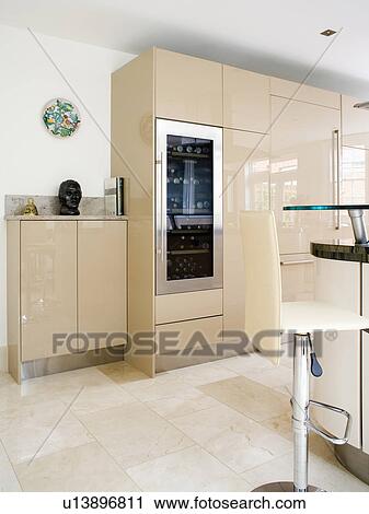 Stock Image - Wine-cooler in large cream fitted unit in modern white kitchen. Fotosearch