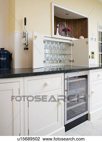 Stock Image - Wine glasses on shelves in kitchen cupboard above refrigerated wine cooler. Fotosearch