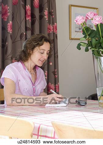 Woman sitting at table and writing in notebook View Large Photo Image Stock Image - Woman sitting at table and writing in notebook. Fotosearch