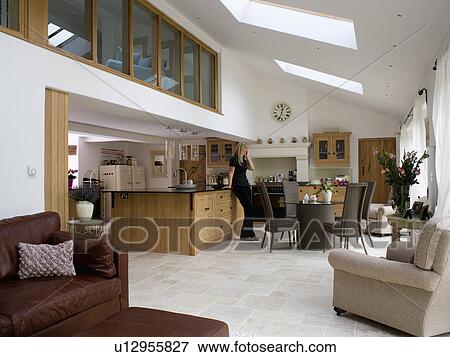 Stock Photo - Woman speaking on the telephone in large open-plan kitchen dining room extension. Fotosearch