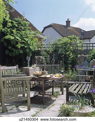 Picture - Wooden benches and table set for lunch on sunny paved patio in country garden. Fotosearch